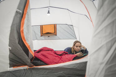 Teenage girl using smart phone while lying in tent - MASF15626