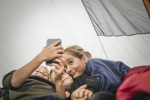 Junge macht Selfie mit Schwestern, während er im Zelt liegt - MASF15628