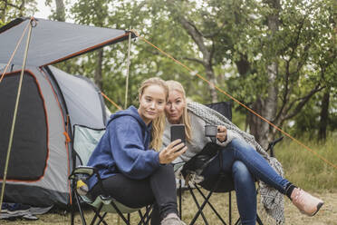 Mutter und Tochter machen ein Selfie mit ihrem Smartphone, während sie auf dem Campingplatz Kaffee trinken - MASF15633