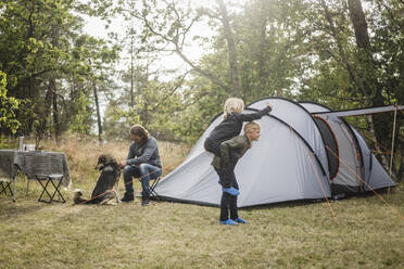 Geschwister spielen, während der Mann mit dem Hund am Zelt auf dem Campingplatz sitzt - MASF15635