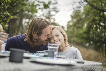 Zärtlicher Vater umarmt Tochter am Tisch auf dem Campingplatz - MASF15645