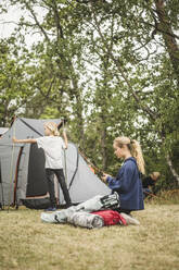 Teenager-Mädchen telefoniert, während die Familie ihr Zelt auf dem Campingplatz aufbaut - MASF15652