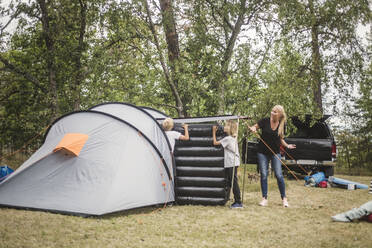 Mutter spricht mit Kindern, die eine Matratze im Zelt auf dem Campingplatz tragen - MASF15654