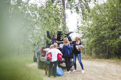 Eltern mit Kindern beim Ausladen des Gepäcks aus dem Auto auf dem Campingplatz im Urlaub - MASF15674