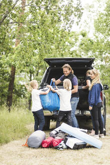 Kinder helfen den Eltern beim Ausladen des Gepäcks aus dem Kofferraum auf dem Campingplatz - MASF15675