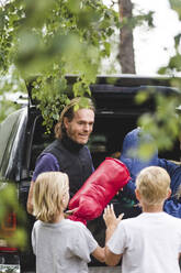 Lächelnder Vater, der den Kindern beim Ausladen aus dem Auto Gepäck gibt - MASF15679