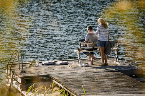 Woman standing by man working on laptop while female executive standing on wooden pier against lake - MASF15724