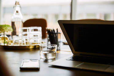 Laptop by drinking glass on conference table in board room - MASF15742