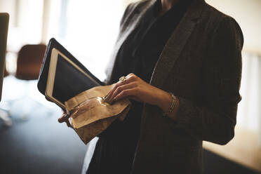 Mittelteil einer Anwältin, die ein Paket und ein digitales Tablet im Büro hält - MASF15744