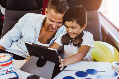 Smiling father and son using digital tablet while sitting in train - MASF15779