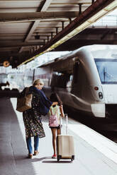 Mutter und Tochter in voller Länge mit Gepäck auf dem Bahnsteig eines Bahnhofs - MASF15804