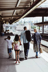 Man with luggage talking to family while walking at train station - MASF15812