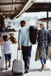 Rückansicht eines Mannes mit Gepäck, der mit seiner Familie am Bahnhof spazieren geht - MASF15814