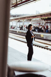 Geschäftsfrau, die ein Mobiltelefon benutzt, während sie auf dem Bahnsteig steht - MASF15828