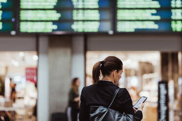 Rückansicht einer Unternehmerin, die ein Smartphone benutzt, während sie am Bahnhof wartet - MASF15829