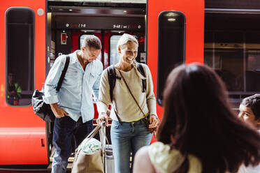 Glückliche Familie mit Gepäck am Bahnsteig vor dem Zug stehend - MASF15836