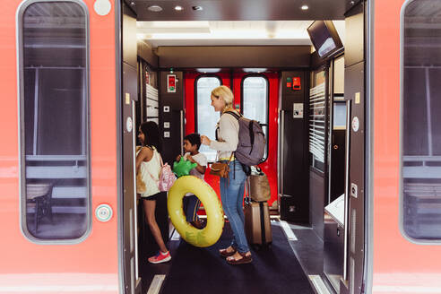 Mother and children with luggage walking in train at station - MASF15839