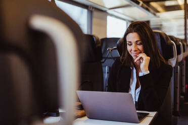 Smiling businesswoman using laptop while sitting in train - MASF15860