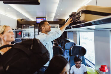 Mittlerer Erwachsener, der während eines Familienausflugs seinen Koffer auf einem Regal im Zug ordnet - MASF15861
