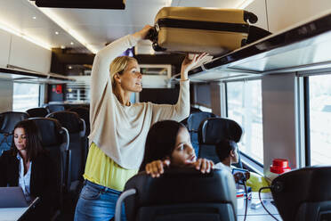 Frau ordnet Gepäck auf einem Regal, während sie mit Kindern im Zug reist - MASF15863