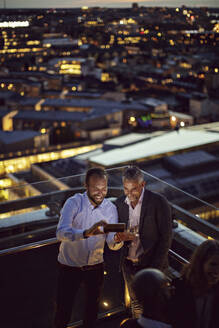 Hoher Blickwinkel von fröhlichen Geschäftsleuten, die ein Selfie mit ihrem Smartphone machen, während sie nach der Arbeit auf der Terrasse stehen, die beleuchtet ist - MASF15880