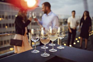 Nahaufnahme von Weingläsern auf einem Tisch mit Geschäftsleuten im Hintergrund auf einer Terrasse während einer Party - MASF15889