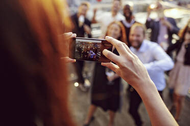 Cropped image of executive photographing coworkers on smart phone at terrace in office party - MASF15902