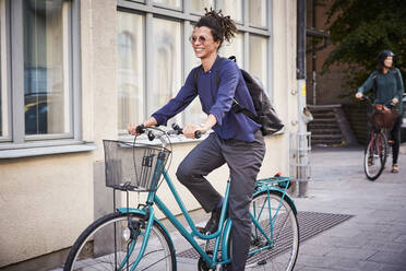 Lächelnde junge Architektin fährt Fahrrad auf der Straße in der Stadt - MASF15934