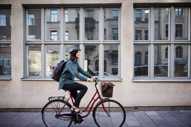 Seitenansicht eines weiblichen Ingenieurs, der auf der Straße neben einem Gebäude in der Stadt Fahrrad fährt - MASF15937