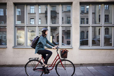 Side view of female engineer riding bicycle on street by building in city - MASF15937