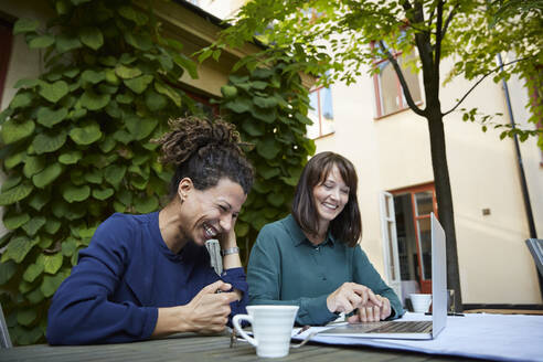 Female architects smiling while working at table in backyard - MASF15946