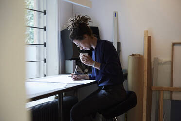 Seitenansicht einer selbstbewussten Architektin bei der Arbeit am Tisch im Büro - MASF15960