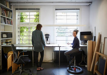 Lächelnde Architektin mit Mitarbeiterin am Tisch im Büro - MASF15968