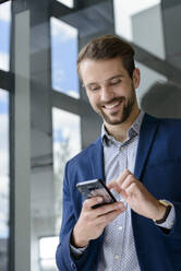 Smiling young businessman using smartphone - BMOF00101