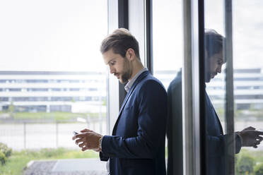 Junger Geschäftsmann mit Smartphone am Fenster - BMOF00102