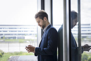 Young businessman using smartphone at the window - BMOF00102