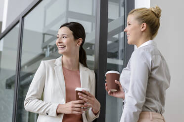 Zwei lächelnde Geschäftsfrauen machen Kaffeepause vor einem Bürogebäude - BMOF00106