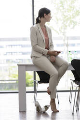 Young businesswoman with smartphone having a break in office - BMOF00107