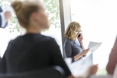 Geschäftsfrau am Telefon im Büro mit Kollegen im Vordergrund - BMOF00121