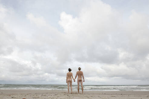 Nude couple standing on the beach, holding hands - EYAF00788