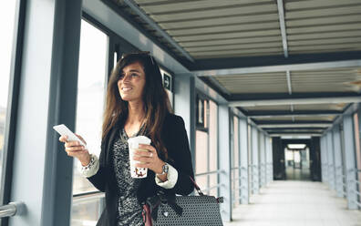 Happy woman looking away while standing on footbridge - CAVF70975