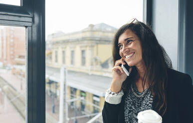 Happy woman talking on smart phone while standing on footbridge - CAVF70978