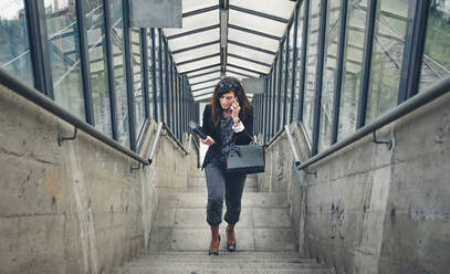 High angle view of woman talking on mobile phone while moving up stairs - CAVF70986