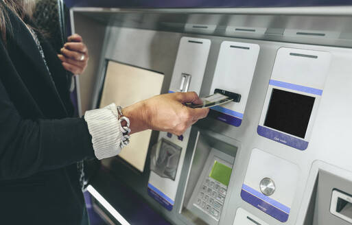 Mittelteil einer Frau, die eine Karte in einen Geldautomaten einführt - CAVF70988