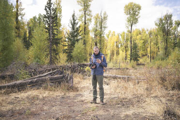 Hiker using mobile phone while standing on field in forest - CAVF71002