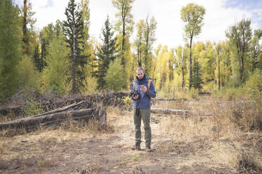 Wanderer, der ein Mobiltelefon benutzt, während er auf einem Feld im Wald steht - CAVF71002