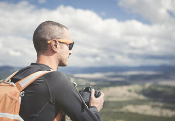 Hiker holding camera while looking at landscape - CAVF71004