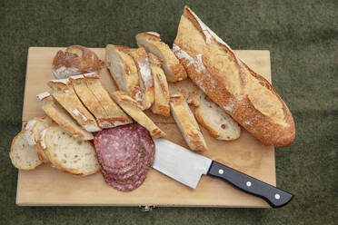 Draufsicht auf Brotscheiben und Salami mit Küchenmesser auf Schneidebrett - CAVF71059