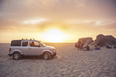 SUV am Strand geparkt, während Freunde bei Sonnenuntergang campen - CAVF71074