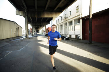 Man jogging on city street under bridge - CAVF71085